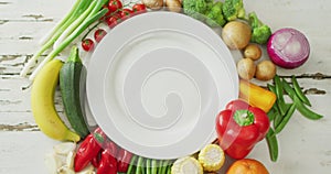 Video of fresh fruit and vegetables around white plate with copy space on wooden background
