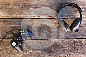 Video game controller and headphones on old wooden background.