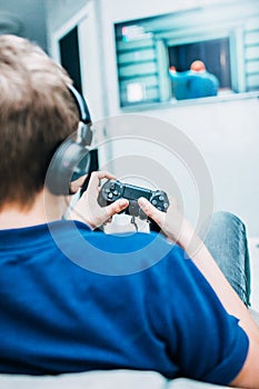 Video games concept - teenage boy playing game with joystick and headphones, enjoying sitting on soft chair in living room. Shoot