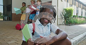 Video of happy african american boy holding books in front of school