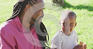 Video of happy african american father and son having picnic on grass