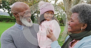 Video of happy african american grandparents, grandfather holding granddaughter in garden