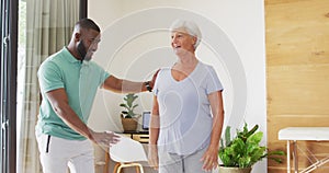 Video of happy african american male physiotherapist exercising with caucasian senior woman