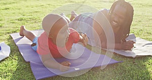 Video of happy african american son and father doing plank on grass and doing high five