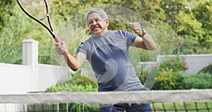 Video of happy biracial senior man jumping with joy during tennis training