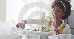 Video of happy biracial woman sorting recycling and smiling at home, with copy space