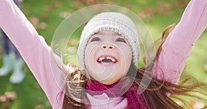 Video of happy caucasian girl in woolly hat and scarf throwing autumn leaves in garden