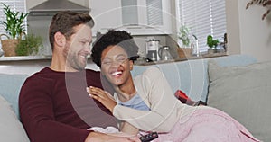 Video of happy diverse couple watching tv on sofa