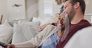 Video of happy diverse couple watching tv on sofa