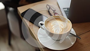 VIdeo of having rest drinking cup of coffee sitting on armchair. Black phone glasses grey laptop on table in office