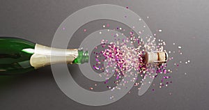 Video of horizontal champagne bottle and cork, with colourful glitter on black background