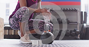 Video of low section of african american woman powdering hands before lifting kettlebell at gym