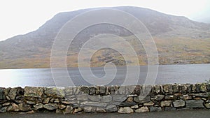 Video, pan across Beautiful lake and Mountains Sun and cloud. Ogwen Cottage, Snowdonia, Wales, wideangle stone wall in foreground