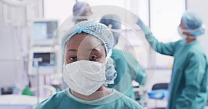 Video portrait of african american female surgeon in mask smiling in operating theatre, copy space