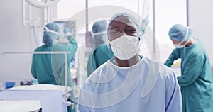 Video portrait of african american male surgeon in mask smiling in operating theatre, copy space