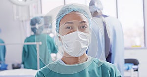 Video portrait of biracial female surgeon in face mask in operating theatre, with copy space