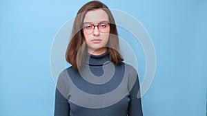 Video portrait of a charming serious student girl with glasses in a blue sweater looking at you and blinking