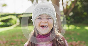Video portrait of happy caucasian girl with missing tooth wearing woolly hat and scarf in garden