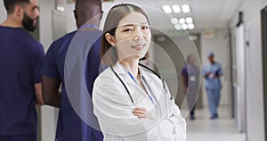 Video portrait of smiling asian female doctor standing in busy hospital corridor, copy space