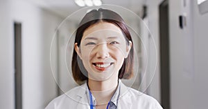 Video portrait of smiling asian female doctor standing in hospital corridor