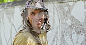 Video portrait of smiling caucasian male artist with dreadlocks painting mural on wall