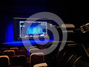 Video shooting in the theater. Digital camcorder with LCD display. Empty auditorium. Blue curtain on stage