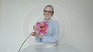 Video shot of shy, pretty blond woman in formal wear sit at table, drink cup of coffee, get big pink flower as present