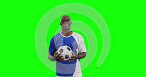 Video of smiling african american male soccer player with ball on green screen background