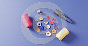 Video of thread snippers, thimble, buttons and reels of cotton on blue background