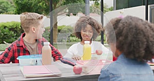 Video of three diverse schoolchildren talking at lunch sitting in schoolyard