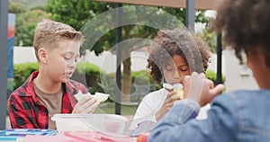 Video of two diverse schoolboys having lunch and talking in schoolyard