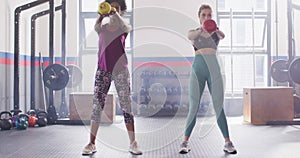 Video of two diverse women working out at a gym doing kettlebell swings in unison