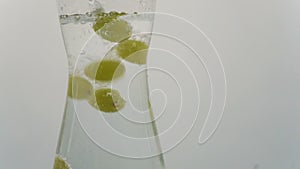 Video of white wine grapes falling into carafe with sparkling water. Wine grapes moving up and down as they are buoyed by air