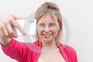 Videocall! Closeup portrait of happy attractive blogger woman in pink blouse standing, holding phone and making selfie and toothy