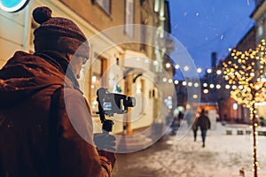 Videographer filming Christmas lights on city street. Man using steadicam and camera for footage. Video shoot