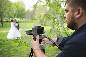 The videographer shootes the marrieds in the garden in the summer
