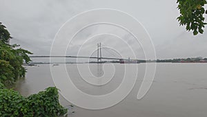 Vidyasagar Setu or Second Hooghly Bridge over the Hooghly River against overcast sky on a rainy day with framing tree in