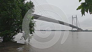 Vidyasagar Setu or Second Hooghly Bridge over the Hooghly River against overcast sky on a rainy day with framing tree in