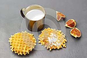 Viennese waffles and fig halves on the table. Milk in a metal mug