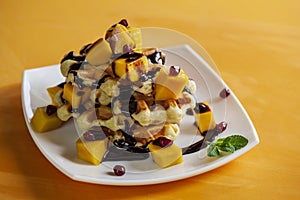 Viennese waffles with ice cream and slices of mango doused with chocolate, on an orange background