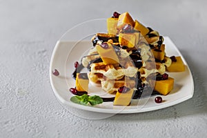 Viennese waffles with ice cream and slices of mango doused with chocolate,in a white plate on a gray background