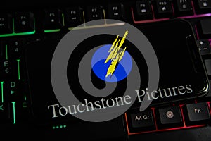 Closeup of mobile phone screen with logo lettering of film production company touchstone pictures on computer keyboard