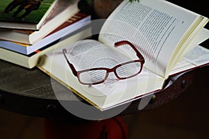 View on open book with red reading glasses and stack of travel books