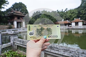 Vietnam 100,000 dong banknote in woman hand on fortress of Van Mieu background, Hanoi, Vietnam