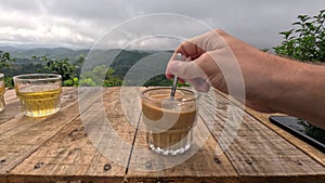 Vietnamese coffee with condensed milk with mountain view. Hand is stirring