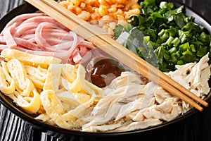 Vietnamese hot noodle soup with chicken, ham, shrimps, egg and herbs close-up in a bowl. horizontal