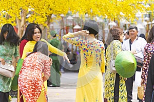 Vietnamese lunar new year. Women wear Vietnam tradition ao dai to take pictures on street with yellow flower apricot in Tet