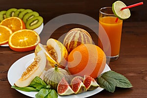 Vietnamese melon, lime, figs, orange, kiwi are on a white plate with a wooden dark background