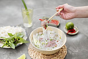 Vietnamese Pho Noodle Soup. Beef with Chilli, Basil, Rice Noodles, Bean Shoots showing noodles picked up with Chopsticks