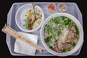 Vietnamese street food, pho bo soup with greens and rice flour noodles, plastic tray served with a large bowl of soup Hanoi street